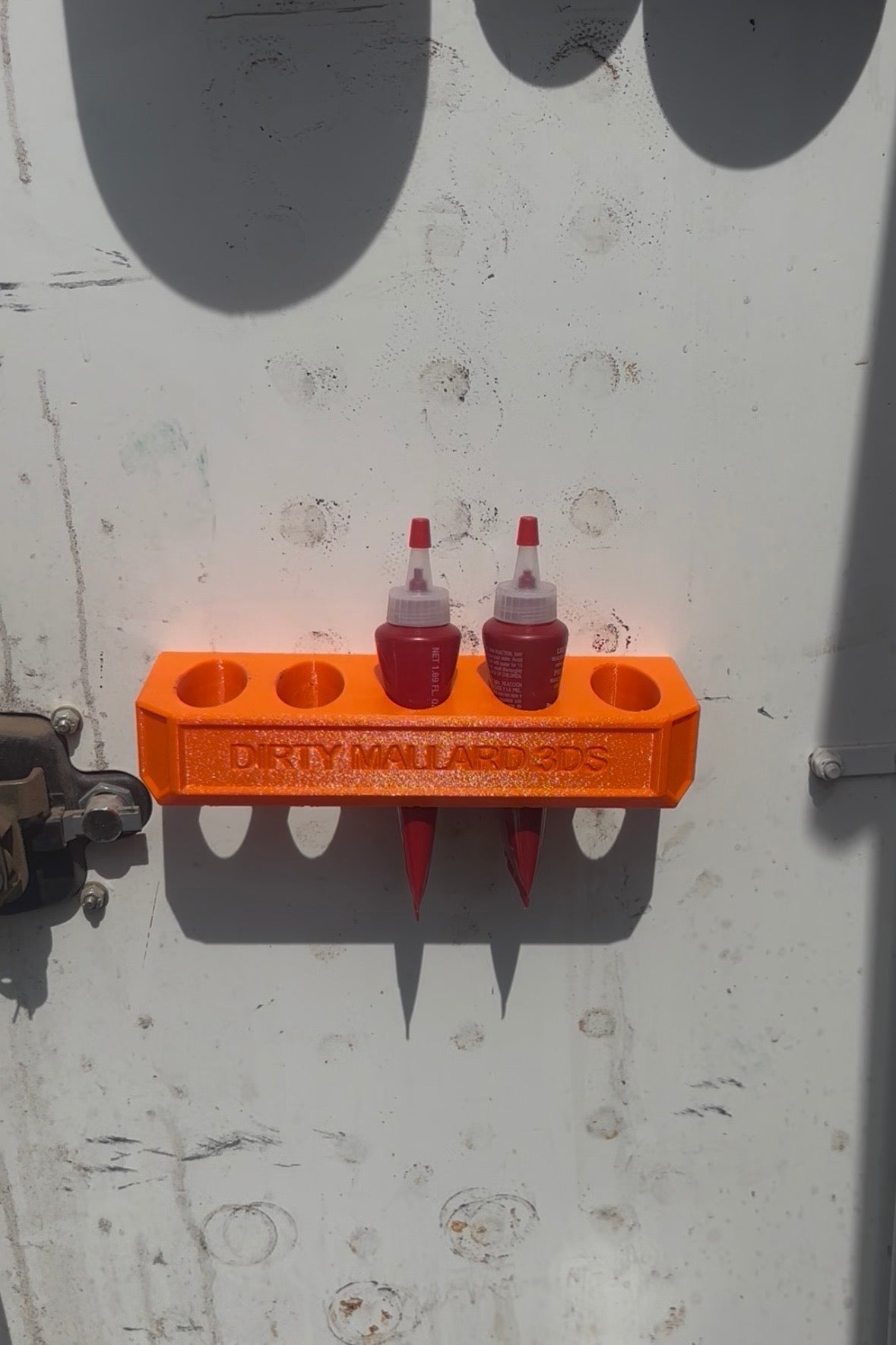 Orange tool holder with two red bottles attached to a metallic surface